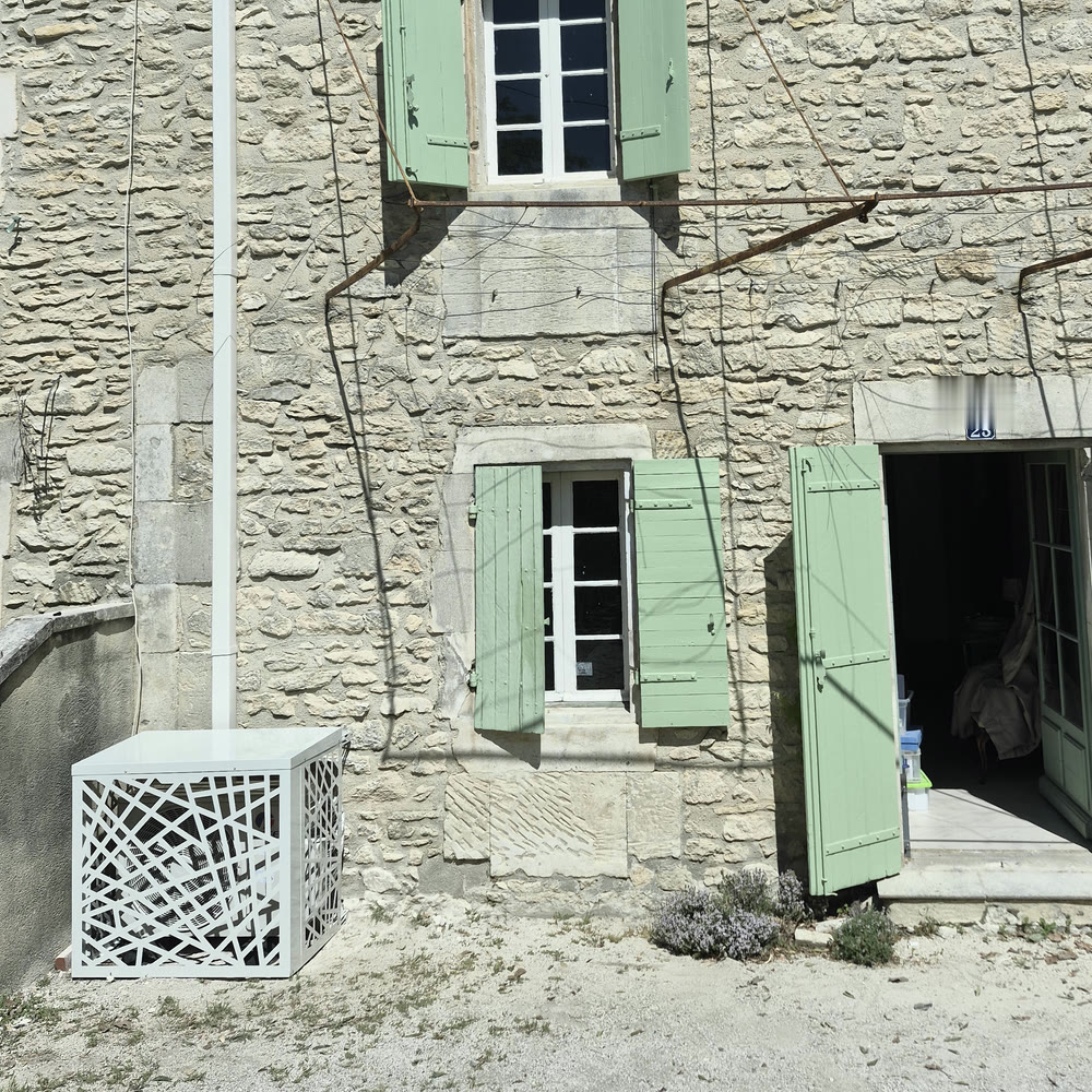 Groupe extérieur dissimulé par un cache ajouré devant une façade en pierre