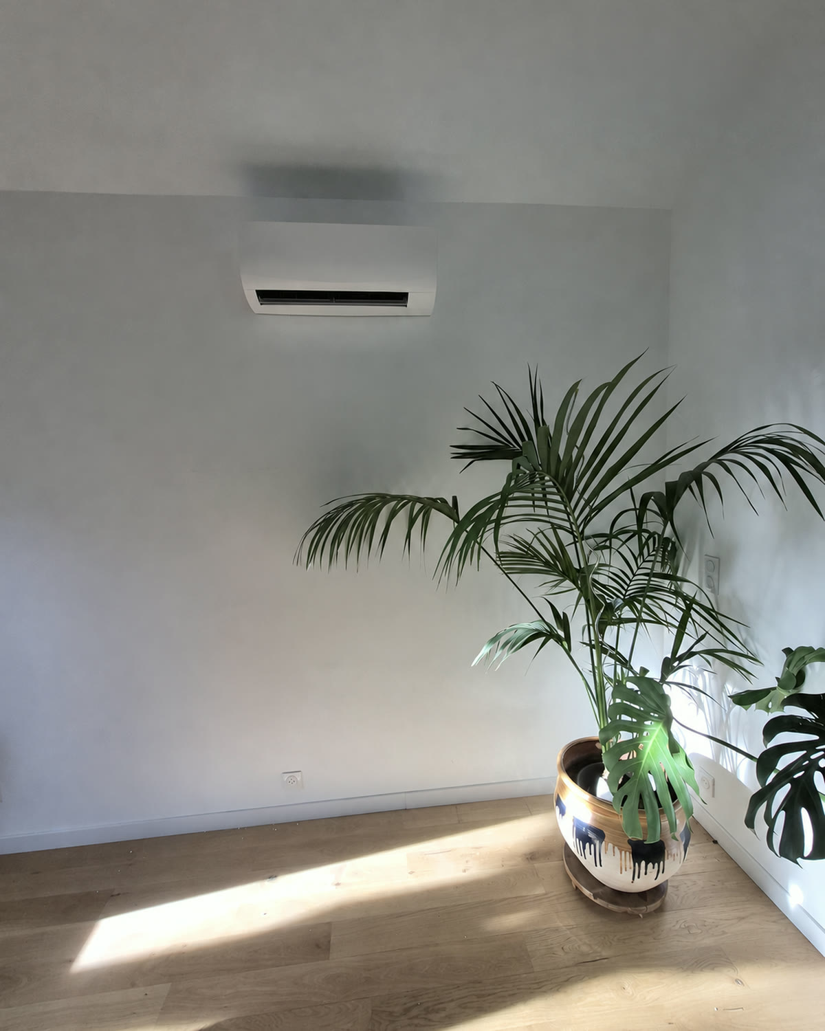 Climatisation murale intégrée dans une pièce lumineuse avec parquet et grandes plantes